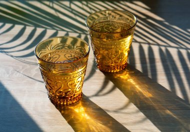 Yaz güneş fotoğrafçılığı. İki sarı cam bardak, parlak güneş ışığıyla aydınlatılmış..