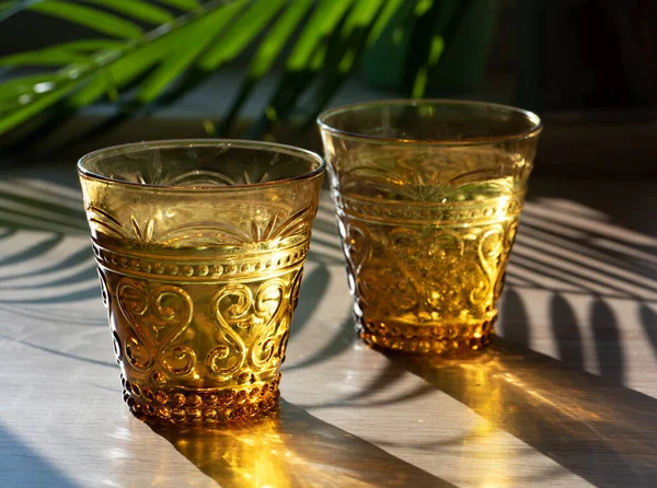 Fotografia solare estiva. Due bicchieri di vetro giallo, illuminati da luce solare brillante . — Foto Stock