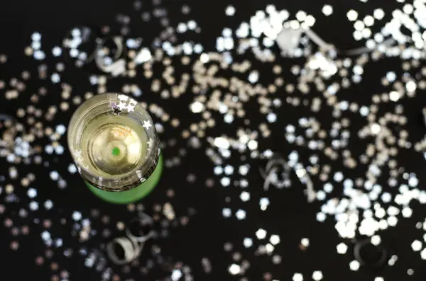 Neon glass with champagne on a black background with silver confetti. — Stock Photo, Image