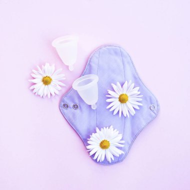 Yeniden kullanılabilir ped ve üzerinde pembe papatyalar olan regl kupası.. 