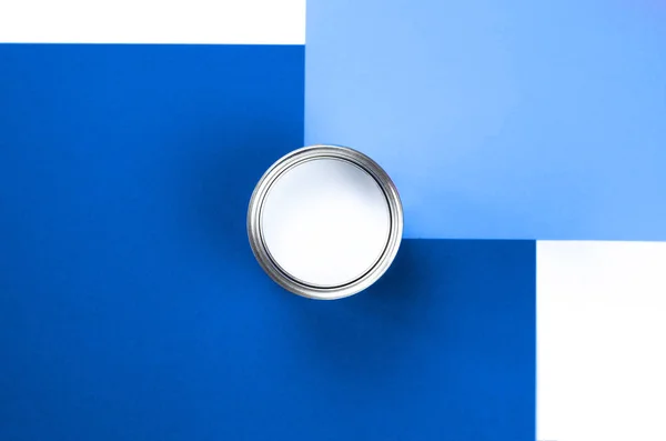 An open can of white paint on a white and blue background.