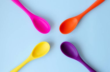 Flat lay of bright multi-colored spoons on a blue background.