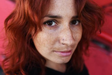 Portrait of a red-haired beautiful girl near the red wall. 
