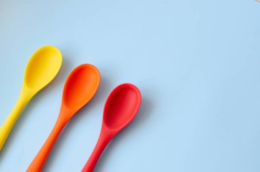 Flat lay of bright multi-colored spoons on a blue background.