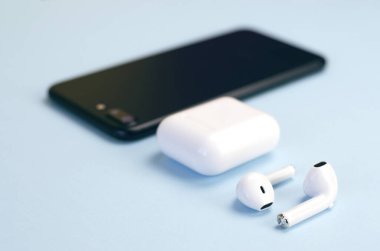 Wireless white headphones with a smartphone on a blue background. New technologies. Trend.