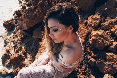 Alışılmadık makyajlı güzel bir kız okyanusta oturuyor. Kadın portresi.