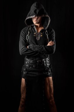Çapraz kollu kapüşonlu gotik giysiler içinde poz veren genç bir oyuncu. Malzemesiz Kraliyet fotoğrafı..