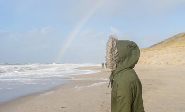 Tanımlanamayan kişi ufukta gökkuşağıyla denize bakıyor.