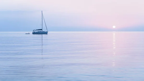Güneşin doğuşu ve mavi sakin suda yüzen tekne