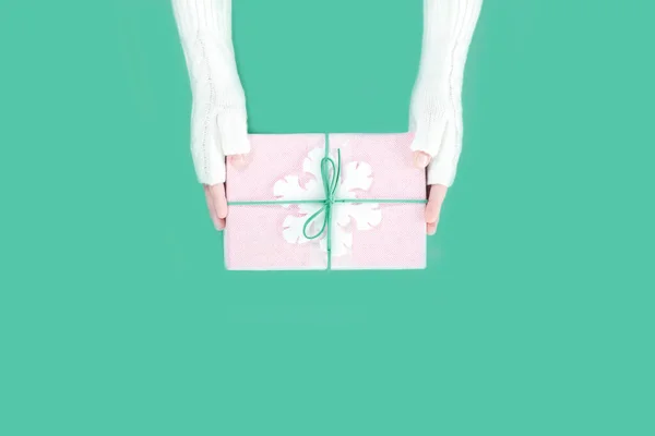 Manos en manoplas con caja de regalo de invierno con copo de nieve sobre verde — Foto de Stock