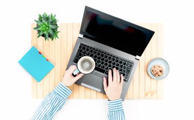 Beyaz masadaki ahşap masa paspasının üzerinde boş ekranı olan dizüstü bilgisayar. Kadın eli çay fincanını tutuyor. Uzaktan öğrenme ya da evden çalışma, çevrimiçi kurslar ya da alışveriş asgari konsept. Evden alışveriş izole