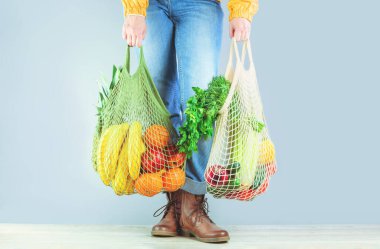 Market teslimatı. Tanınmayan kız elinde meyve ve sebzelerle dolu iki alışveriş çantası tutuyor. Çevre dostu, sorumluluk sahibi bir yaşam tarzı ve alışveriş. Sağlıklı beslenme, sıfır atık konsepti. Uzayı kopyala Bağış