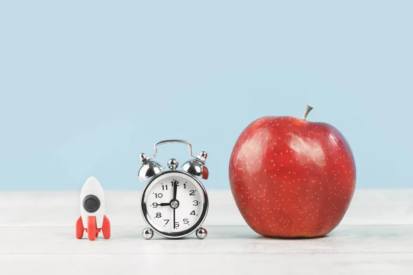 Organized office or school desk. Toy rocket and alarm clock and big red apple on grey wooden desk. Copy space for back to school or education knowledge craft and innovative startup concept