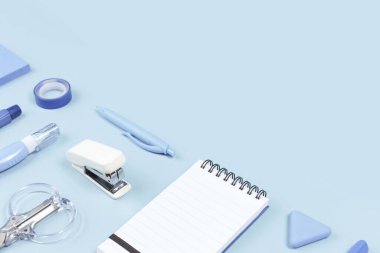 Sınır olarak pastel arka planda çeşitli ofis ve okul beyaz ve mavi kırtasiye ürünleri. Okula dönmek ya da eğitim ve zanaat konsepti için fotokopi alanı olan bir daire. Mavi monokrom bayrağı