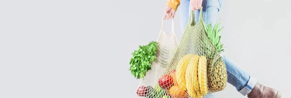 Delivery of grocery. Unrecognizable girl holds two mesh shopper bags with fruit and vegetables. Eco friendly responsible lifestyle and shopping. Healthy eating, zero waste concept. Copy space banner