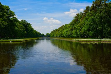 Almanya 'nın Münih kentindeki bir parkta güneşli bir bahar gününde bir gölet ve kanal büyük bir perspektif sunuyor.
