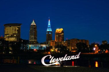CLEVELAND, OH - OCTOBER 4, 2019: The newest of the script Cleveland signs stands across the Cuyahoga River from the downtown skyline. clipart