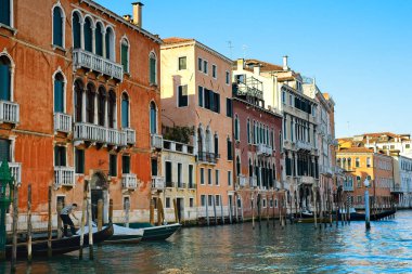 Venedik, İtalya - 2 Haziran 2019: Geleneksel çizgili tişörtü giyen yalnız bir gondolcu, Grand Canal 'daki yıpranmış, eski püskü binaların önünde demirli olan gondoluyla ilgilenir..