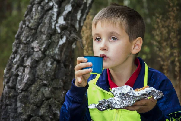 Menino no outono na floresta bebendo chá de uma xícara de steami — Fotografia de Stock