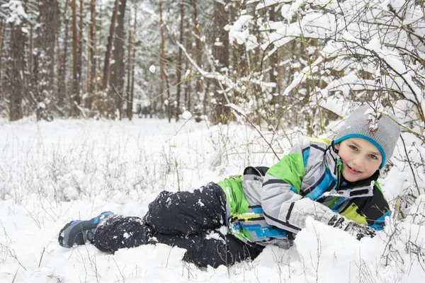 In winter, snow-covered pine forest boy lies near the snowdrift. — Stock Photo, Image