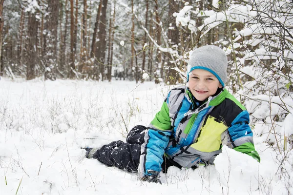 Взимку засніжений сосновий ліс хлопчик лежить біля снігового дрейфу . — стокове фото