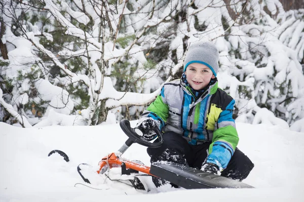 Im Winter sitzt der schneebedeckte Waldjunge auf einem Schlitten. — Stockfoto