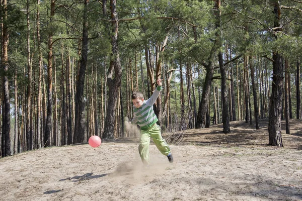 Solig sommardag i skogen pojken sparkar bollen foten, cirka en — Stockfoto