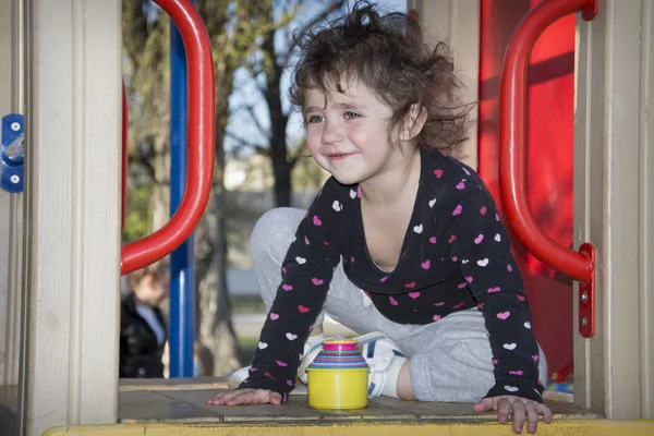 Im Frühling auf dem Spielplatz ist ein lächelndes kleines Mädchen. — Stockfoto