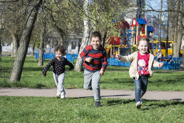 Primavera begaayut niños en la hierba cerca del parque infantil . —  Fotos de Stock