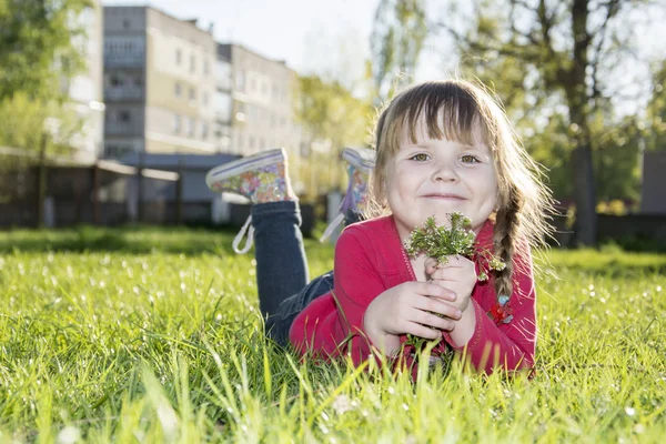 Frühling im Park auf dem Rasen ist ein kleines lustiges Mädchen. — Stockfoto