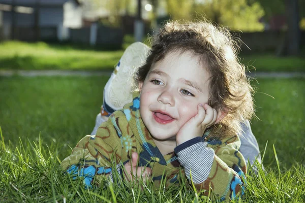 Våren i parken på gräset är en liten rolig flicka. — Stockfoto