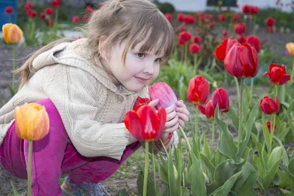 Frühling im Garten eines schönen kleinen Mädchens, das sitzt und riecht — Stockfoto