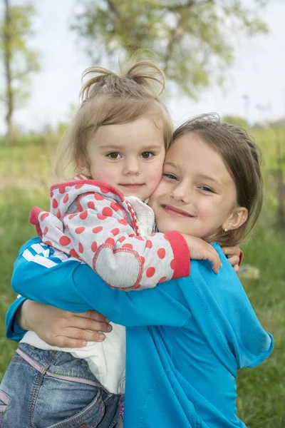 Lente in de straat grote zus omarmt de jongere. — Stockfoto