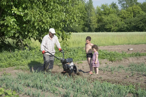 Lente in de tuin man ploegen land motor-blok kleine zoon en — Stockfoto