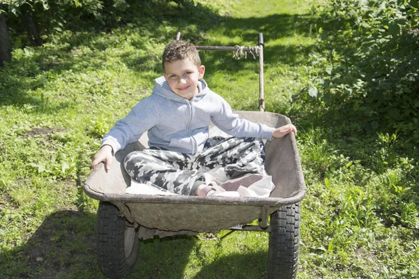 Frühling im Garten in einer Schubkarre sitzt ein kleiner lockiger Junge. — Stockfoto