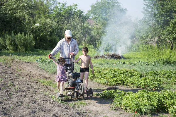 Primavera en el hombre del jardín arando la tierra motor-bloque pequeño hijo y — Foto de Stock