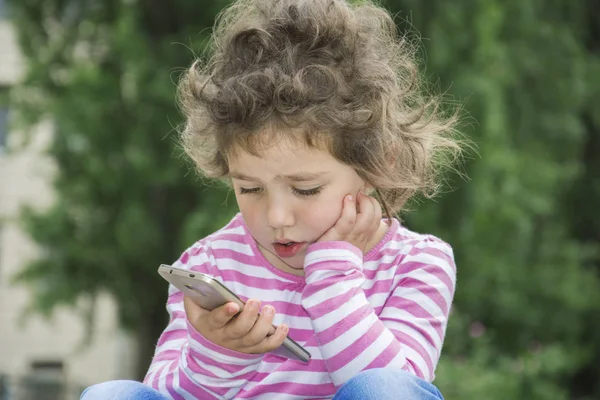Letní venkovní kudrnatá dívka sedí a zírá něco na ph — Stock fotografie