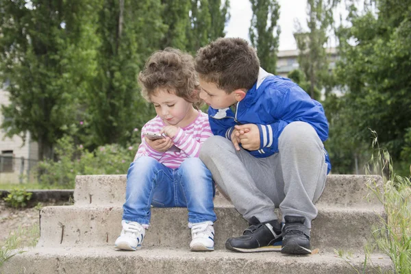 V létě venku sedí malé kudrnatou dívku a chlapce — Stock fotografie