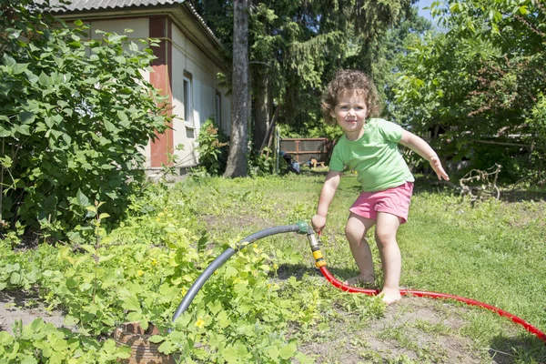 En verano, el jardín incluye una niña con un grifo de manguera . — Foto de Stock