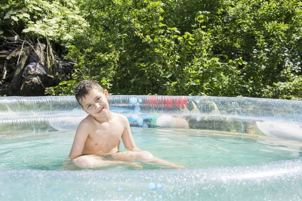 Om sommeren i hagen bader gutten i oppblåsbart basseng. . – stockfoto