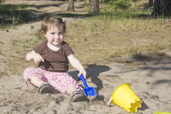 In summer, a little girl in a pine forest digs a shovel. — Stock Photo, Image