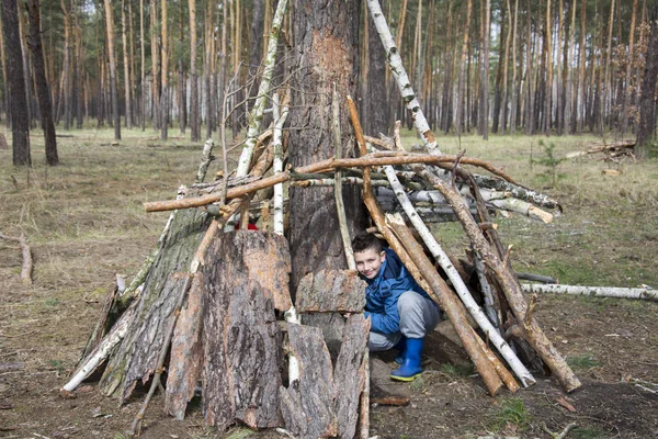 松の森の春、少年はスティックの小屋を建てください。. — ストック写真