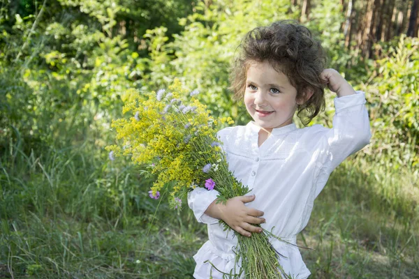 In estate, nella foresta, una piccola ragazza riccia tiene un fiore e — Foto Stock