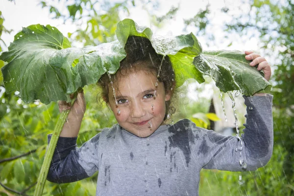 En un día lluvioso de verano, una niña se esconde de la lluvia bajo una —  Fotos de Stock