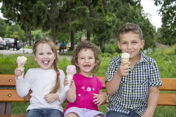 No verão no parque, as crianças sentam-se em um banco e comem gelo c — Fotografia de Stock