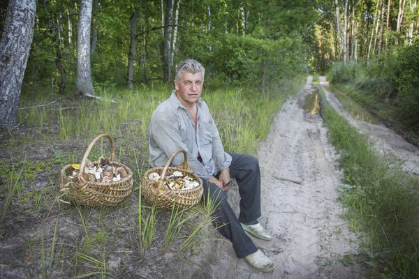 V létě, sedí muž s dvěma košíky hub v — Stock fotografie