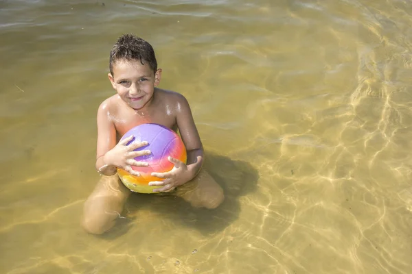 En verano, en un día soleado y brillante, un niño en el río juega con —  Fotos de Stock