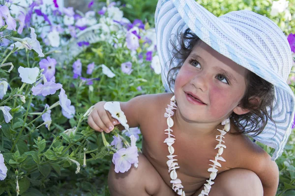 W lecie mała dziewczynka w kapeluszu z korale z muszli siedzi w pobliżu — Zdjęcie stockowe