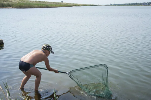 En el verano en el lago el niño atrapa el pez con una servilleta —  Fotos de Stock