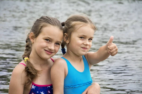 In the summer on the river, two small sisters in bathing suits a — Stock Photo, Image
